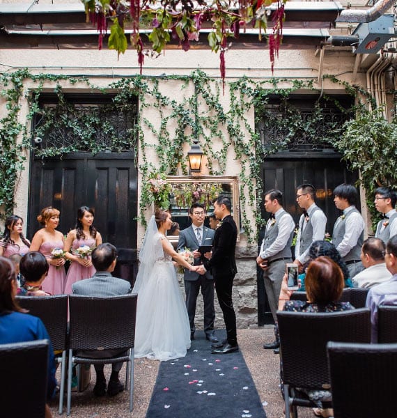 A bride and groom stand close in a courtyard at Brix & Mortar, her veil flowing elegantly, with ivy and warm lighting framing the moment.