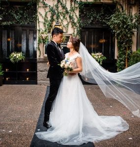 A bride and groom stand close in a courtyard at Brix & Mortar, her veil flowing elegantly, with ivy and warm lighting framing the moment.