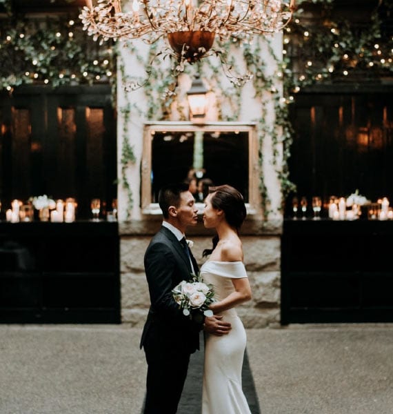 A couple shares a tender moment under the chandelier at their Brix & Mortar wedding, surrounded by fairy lights and ivy in Vancouver