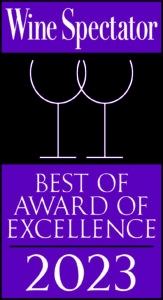 An image displaying the 'Wine Spectator Best of Award of Excellence 2023' in bold white and purple text, with a graphic of two stylized wine glasses above the title, signifying high recognition in the wine industry and award gained by Brix & Mortar restaurant.